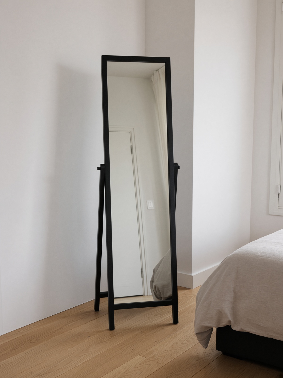 A black standing mirror in a pale bedroom.