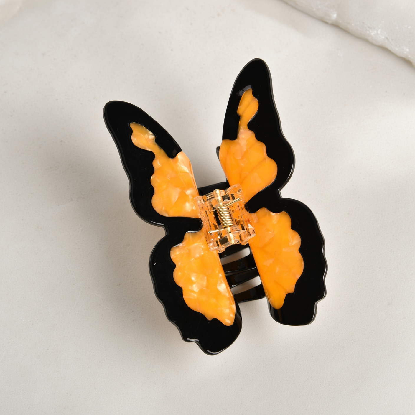 A black and amber butterfly hair claw on a pale stone surface.